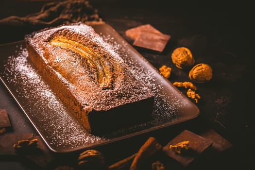 Homemade vegan banana bread or cake with nuts, chocolate and cinnamon on brown background