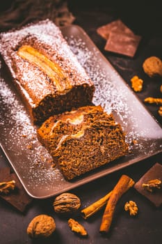 Homemade vegan banana bread or cake with nuts, chocolate and cinnamon on brown background