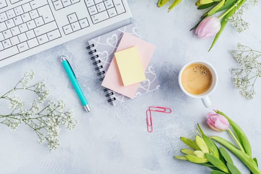 Workplace with cup of coffee, empty notebook, keyboard, supplies and flowers in bright tone