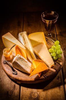 Cheese platter, assortment of different cheeses with glass of red wine, grapes on wooden table