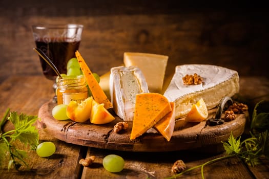 Cheese platter, assortment of different cheeses with glass of red wine, grapes on wooden table