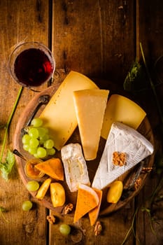 Cheese platter, assortment of different cheeses with glass of red wine, grapes on wooden table