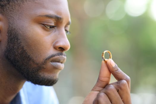 Sad black husband doubting holding wedding ring in a park