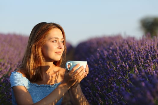 Happy woman drinking coffee contemplaing sunset in lavender field