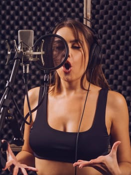Beautiful woman singing into a large diaphragm microphone in a professional recording studio.