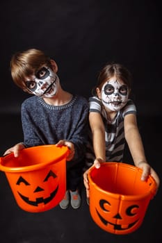 Two children with skull makeup holding pumpkin pails at Halloween.