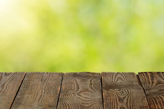 Background with blurred green leaves and empty wooden planks in the foreground. For product demonstrations, free space, layout, mockup, perspective board, background board.