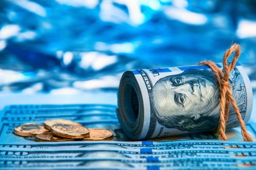 Dollars. A roll of hundred-dollar bills and scattered gold coins lying on the bills on a blue background with a side. Blue style.