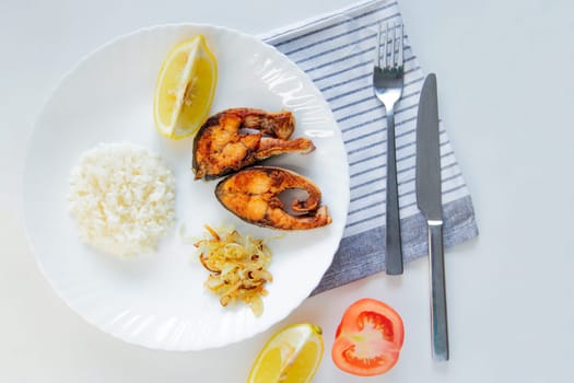Fried fish with onions, rice and lemon lies on a plate, on a waffle towel and cutlery on a white background. High quality photo