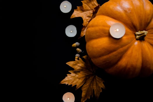 An orange pumpkin with leaves, acorns and candles on a black background. High quality photo