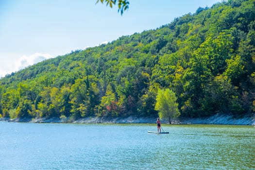 A girl is floating on a board on the river, in the background there are mountains overgrown with trees. High quality photo