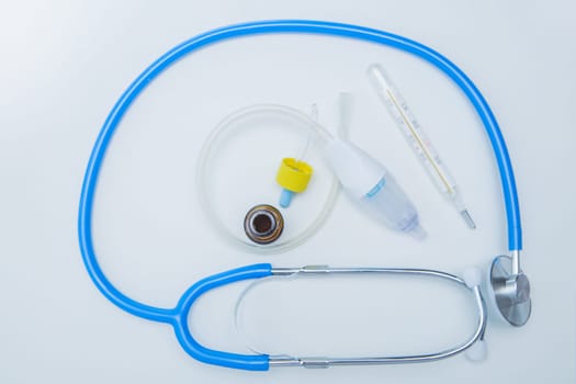 The stethoscope lies on a white background around, inside it is a baby aspirator, nose drops and a thermometer. High quality photo