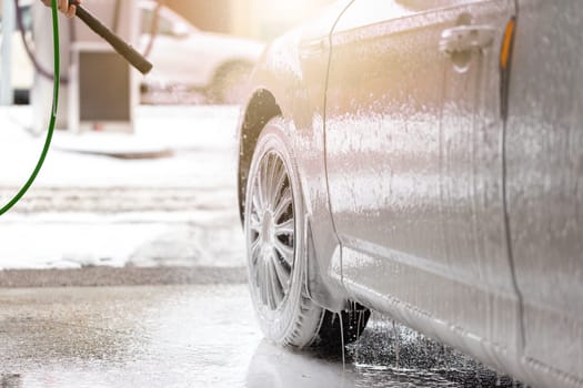 Car cleaning with high pressure in exterior carwash. Washing automobile with manual equipment with soap on sunlight. Purifying vehicle touchless with wet sprey.