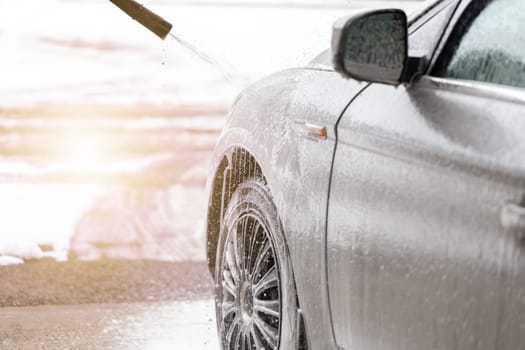 Purifying automobile with touchless technology in exterior carwash. Cleaning car with high pressure on sunlight. Washing vehicle manual with water and soap.