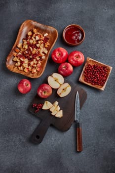 Still life with fresh lingonberries, red appples with knife on black cutting board and  homemade jam on wooden bowl on dark background. Top view. Autumn harvest, Home canning.