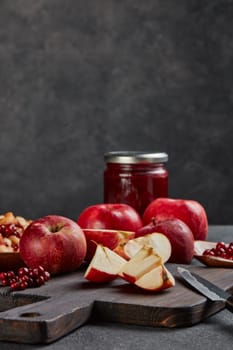 Still life with fresh lingonberries, red appples with knife on black cutting board and jar of homemade jam on dark background with copy space. Autumn harvest, Home canning.