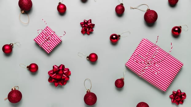Gray background with two Christmas gift box presents, small red Christmas balls or sphere toys, ribbon bows for fir tree. Concept for festive greeting card or invitation for Christmas eve celebration
