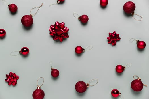 Pattern on gray background with small red Christmas balls or sphere toys, ribbon bows for fir tree. Concept for festive greeting card or invitation for Christmas eve celebration. High quality photo