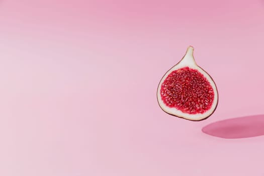 Fresh tasty fig fruit halve levitation with shadow on pink background. Cross section of fig falling down or fly. Vegan desert concept. Shadow of flying healthy eating food. High quality colorful photo