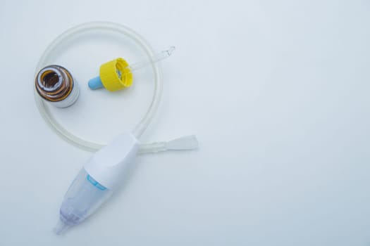 The children's aspirator lies rolled up in a ring on a white background, inside it are drops from a runny nose with a pipette. . High quality photo