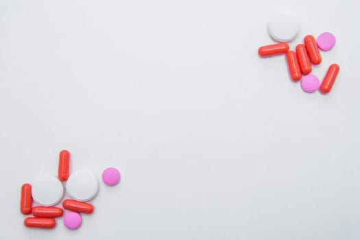 Tablets and capsules of white and pink color lie in opposite corners of the photo with space for text on a white background. High quality photo