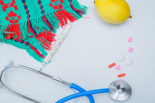 A warm winter scarf, a thermometer, a lemon, a stethoscope and pills with capsules lie on a white background. High quality photo