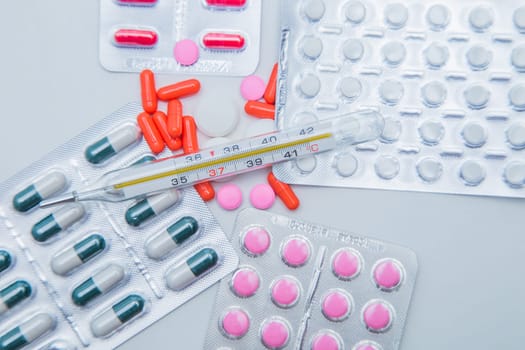 Tablets in capsules in packages and without lie on the entire surface of the photo with a thermometer on top. . High quality photo