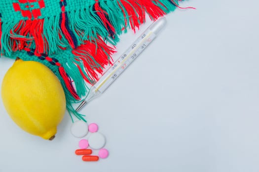 A warm winter scarf, thermometer, lemon and pills with capsules lie on the side on a white background with a place for text. High quality photo
