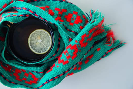 A cup of tea with lemon wrapped in a green and red scarf. . High quality photo