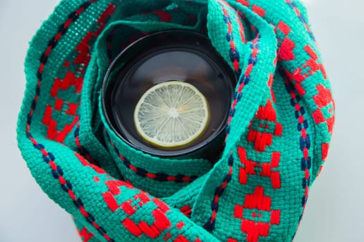 A cup of tea with lemon wrapped in a green and red scarf. . High quality photo