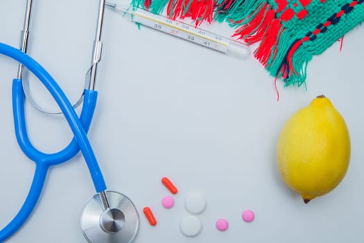 A warm winter scarf, a thermometer, a lemon, a stethoscope and pills with capsules lie on a white background. High quality photo