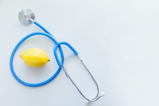 The blue stethoscope lies on a white background with a lemon in the middle. High quality photo