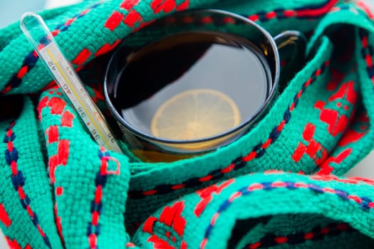 A cup of tea with lemon wrapped in a green and red scarf with a thermometer. High quality photo
