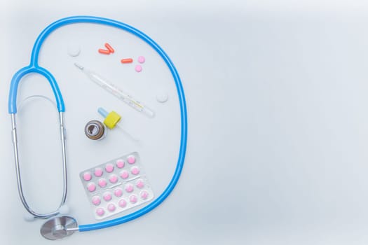 The stethoscope lies on a white background in a circle, inside it is a thermometer, medicines and drops from a runny nose. . High quality photo