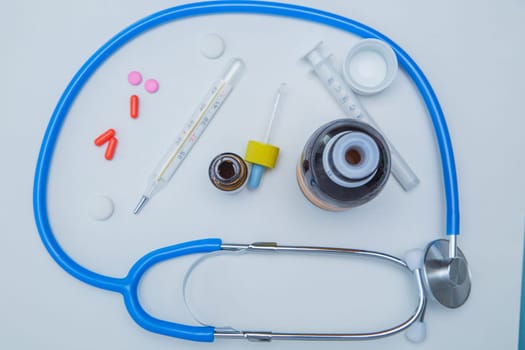 The stethoscope lies on a white background around, inside it is a thermometer, medicines, medicine and drops from a runny nose. High quality photo