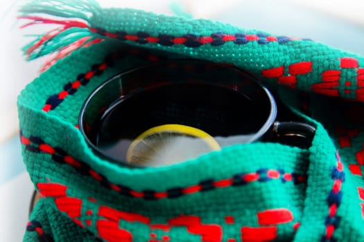 A cup of tea with lemon wrapped in a green and red scarf. . High quality photo