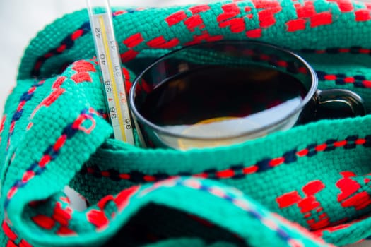 A cup of tea with lemon wrapped in a green and red scarf with a thermometer. High quality photo