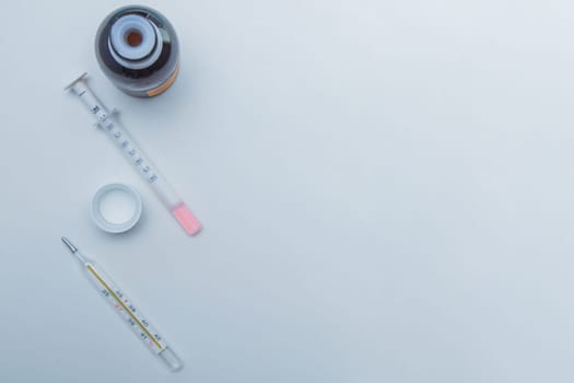 A medicine with a measuring syringe and a thermometer lies on the side against a white background. High quality photo
