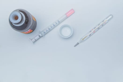 A medicine with a measuring syringe and a thermometer lies a white background. High quality photo
