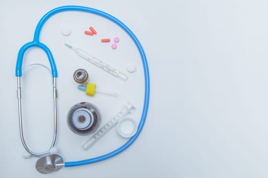 The stethoscope lies on a white background around, inside it is a thermometer, medicines, medicine and drops from a runny nose. High quality photo