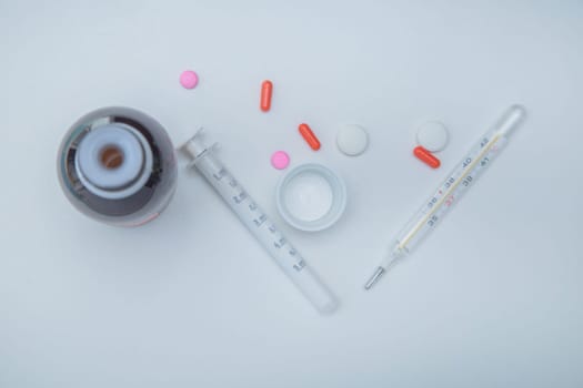 A medicine with a measuring syringe, tablets and capsules and a thermometer lies on the side against a white background. High quality photo