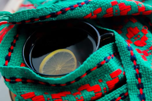 A cup of tea with lemon wrapped in a green and red scarf. . High quality photo