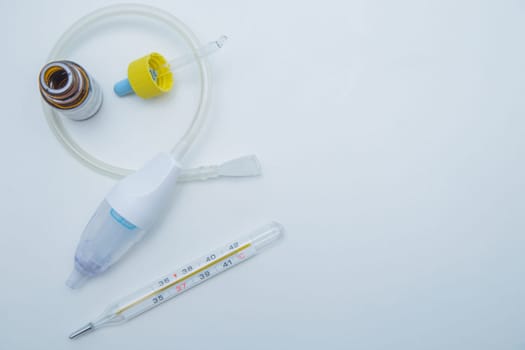 The children's aspirator lies rolled up in a ring on a white background, drops from a runny nose with a pipette in its interior, a thermometer with a place for text lies on the side. . High quality photo