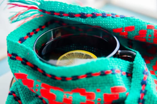 A cup of tea with lemon wrapped in a green and red scarf. . High quality photo