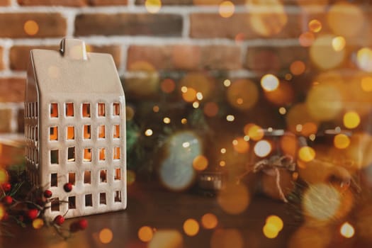 Christmas candle in form of house or home, symbol of family celebration, blurred background with Christmas fir tree festive decorations, lights, garlands. Festive mood at home. High quality photo