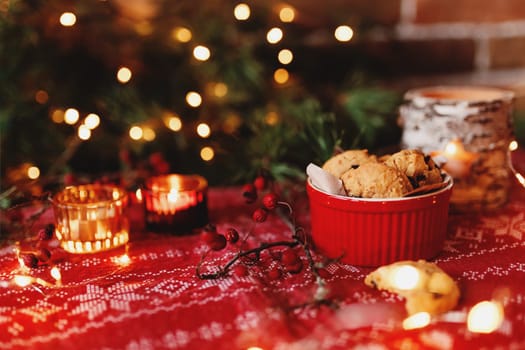 Red festive bowl full with tasty Christmas chocolate cookies, blurred background with Christmas fir tree decorations, lights, garlands and candles. Festive mood at home. High quality photo