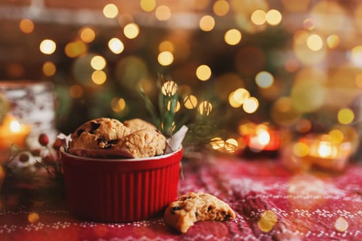 Red festive bowl full with tasty Christmas chocolate cookies, blurred background with Christmas fir tree decorations, lights, garlands and candles. Festive mood at home. High quality photo