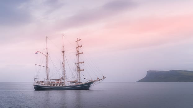 Early morning, beautiful tall ship anchored near Northern Ireland coast, covered in haze with Fair Head in far distance, Ballycastle