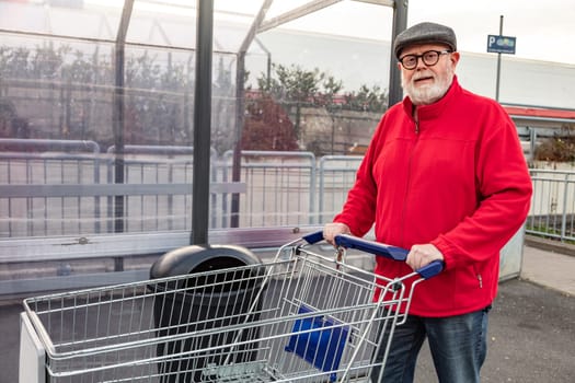 Smiling senior with a cap and red jacket pushing a shopping cart