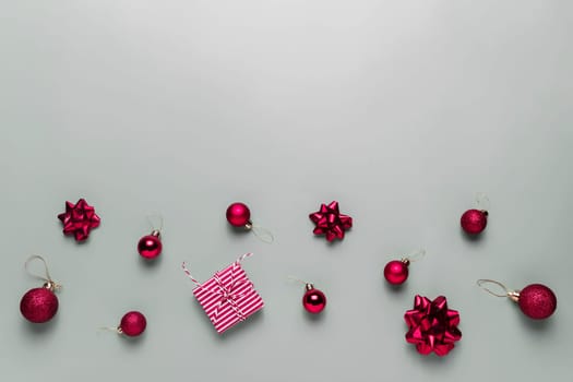 Gray background with pink Christmas gift box present, small red Christmas balls or sphere toys, ribbon bows for fir tree, other decorations. Christmas sales, shopping or greeting card or invitation